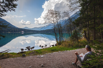 Urlauber entspannt sich mit einem Buch auf einer Bank am Rundwanderweg des Antholzer Sees - mit...
