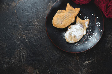 Black plate with traditional japanese taiyaki cakes, top view on a dark-brown stone background, horizontal shot with copyspace