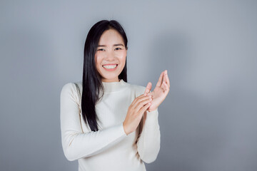 Smiling asian woman wears cream sweater standing on gray background
