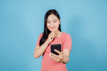 Portrait of smiling Asian woman with long dark hair  taking a selfie on blue background