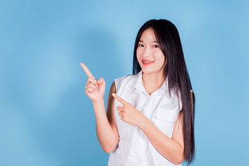 Portrait of smiling asian woman pointing finger to the side on blue background