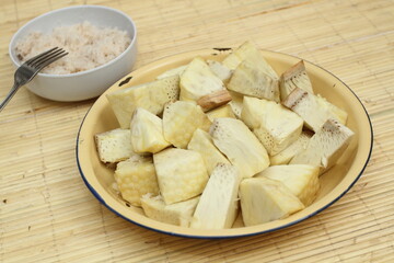 Steamed breadfruit (Artocarpus altilis) slices served on plate. A bowl of grated coconut on the background