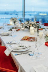 Festive table setting for a wedding or banquet with a panoramic view of the city, red chairs.