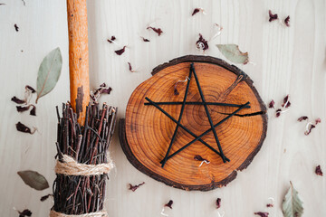 Hand made DIY besom broom and black pentagram on a white wooden table. Witchy flat lay of ritual witchcraft items