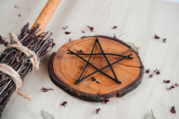 Hand made DIY besom broom and black pentagram on a white wooden table. Witchy closeup of ritual...