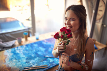 A young sexy and attractive female artist in her studio  is excited about roses she got. Art, painting, studio