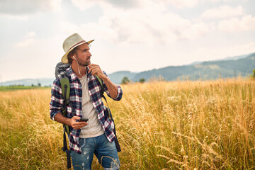 A young man is enjoying the music while hiking a meadow. Hiking, nature, activity