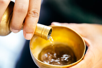 Hand person is pouring water with brass cup. Concept of making merit and dedicating charity in...