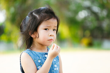 Portrait Asian child girl eating snack at outdoors. Kid hungry after playing in public park. Children is feeling hot and sweating on her face due to the hot weather. Baby aged 5 years old. Empty space