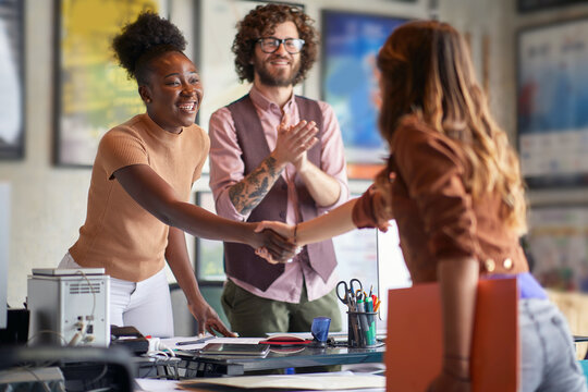 young caucasian male clapping hands, satisfied due to new good business deal, watching two females, multiethnic, shaking hands