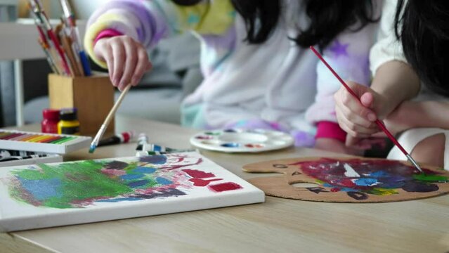 Two girls painting with water color while spending leisure time together at home.