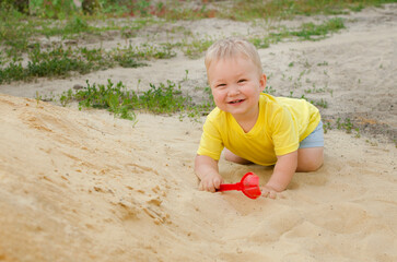 Cute little boy child plays and smiles in the sandbox in the summer in a yellow T-shirt. Childhood, joy, playful concept