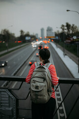 a girl in a red jacket looks at the highway with cars