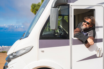 Cheerful happy toutist man smile and admire outside the driver windows of his modern white camper car motorhome. People and travel lifestyle or renting vehicle for summer vacation holiday