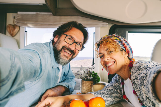 Happy and cheerful confident man and woman couple smile and have fun taking selfie picture inside a cozy modern camper van. Tourist and vanlifers people enjoy freedom happiness together on vacation