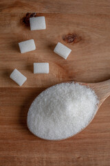 Granulated sugar and sugar cubes in wooden spoon on wooden background	