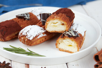 Beautiful delicious french eclairs set with original cream decor on white plate on wooden background, tasty colorful dessert profiteroles