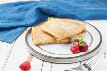 Crepes stuffed on plate, thin pancakes, blini, white wooden table