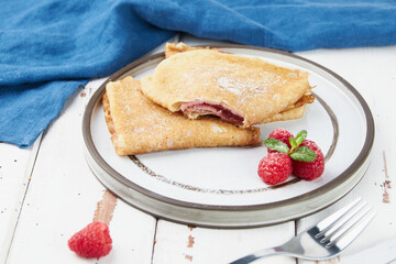 Crepes stuffed on plate, thin pancakes, blini, white wooden table