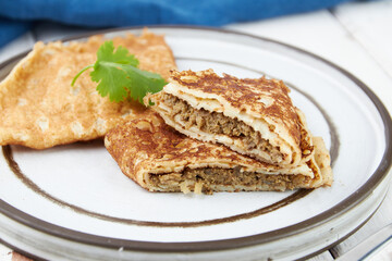Crepes stuffed on plate, thin pancakes, blini, white wooden table