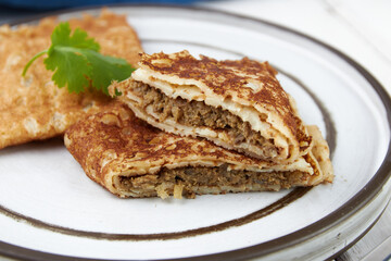 Crepes stuffed on plate, thin pancakes, blini, white wooden table