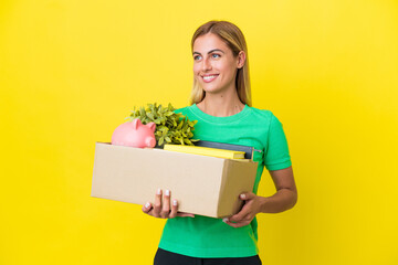 Young Uruguayan girl making a move while picking up a box full of things isolated on yellow...