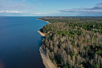 Aerial view of the coastline of the Gulf of Finland. Sandy coast and forest belt. Treetops, blue sky.