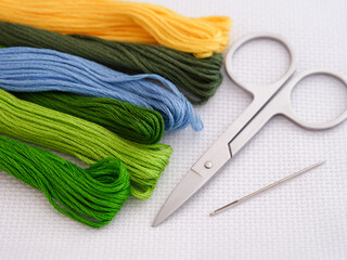 Colorful cross stitch embroidery threads on a canvas with scissors and a needle next to them