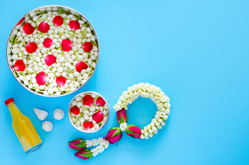 Songkran festival background with flowers in water bowls, jasmine garland, scented water and marly limestone for blessing on blue background.