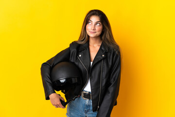 Fototapeta premium Woman holding a motorcycle helmet isolated on yellow background thinking an idea while looking up