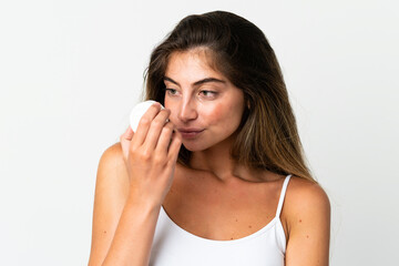 Fototapeta premium Young caucasian woman isolated on white background with moisturizer and smelling it