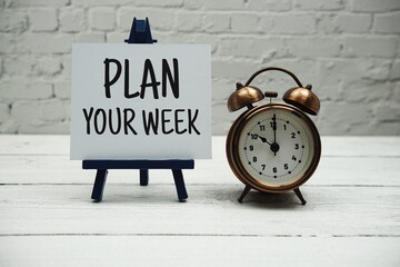 Plan Your Week text and alarm clock on white brick wall and wooden background