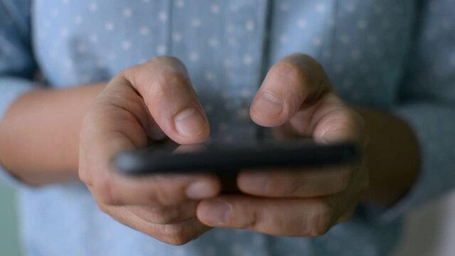Close up hands of a woman in blue shirt typing on mobile smartphone's touchscreen. Texting message on mobile app. Chatting on social communication online. 