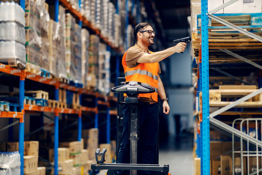 A smiling supervisor on forklift scanning boxes with qr and bar code scanner in warehouse.