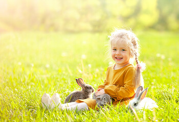 the girl is sitting on the sunny lawn among the rabbits, smilling and looking at the camera	