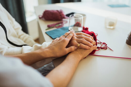 Cropped image of female caregiver stacking hands on senior woman at retirement home
