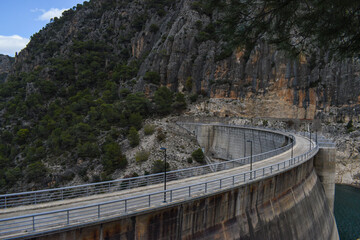 Curving hydro electric dam with road on top and sheer rock face in the background