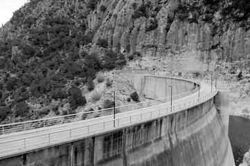 Curving hydro electric dam with road on top and sheer rock face in the background