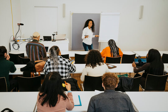 Smiling professor teaching students while standing by flipchart in classroom