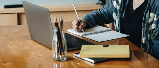 Cropped photo of woman writing making list taking notes in notepad working or learning on laptop...