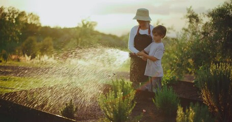 Grandmother and young grandson spending quality time together in the garden, watering garden beds in the backyard at sunset