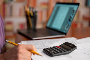 Male accountant in the office uses a calculator and writes data in a notebook. Profit analysis, taxes and payments calculations, preparation of financial statements concept