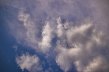 white cloud with gray-shaded tips blown by the winds under a blue sky covered by a thin veil of clouds.