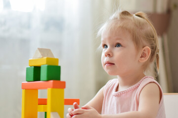 A small child is playing at a table with a wooden construction kit. A game with cubes. Children's games