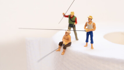 トイレットペーパーの上で魚釣りをする３人の男の人のフィギュア