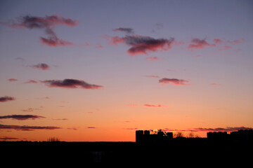 Landscape, with disturbing red sunset in the sky and few clouds above dark skyline and some buildings contours at far