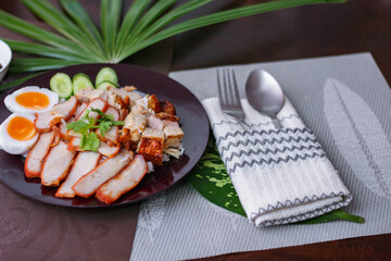Steamed rice and red pork, crispy pork in a black plate Served with dipping sauce and dark soy sauce Place it on a black wooden table.