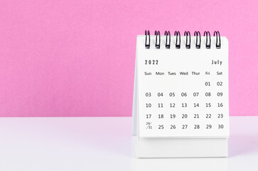 July 2022 desk calendar on white table with pink background.