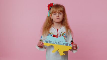Angry toddler Ukrainian girl kid in embroidery dress protesting war conflict raises banner with inscription massage text on map Hands Off Ukraine on pink background. Peace, no war, stop aggression