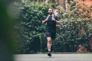 Determined young man running outside in the park. Fit boy doing exercise outdoor. Beautiful sporty...